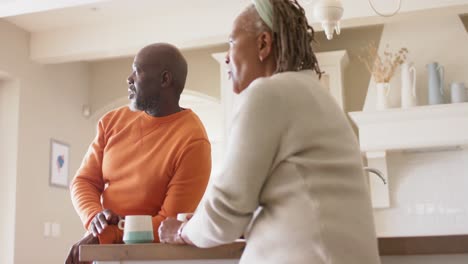 Fröhliches-Afroamerikanisches-Seniorenpaar,-Das-In-Der-Küche-Redet-Und-Kaffee-Trinkt,-Zeitlupe