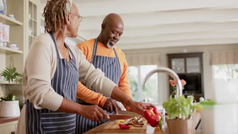 Fröhliches-Afroamerikanisches-Seniorenpaar-In-Schürzen,-Das-Essen-In-Der-Küche-Zubereitet,-Zeitlupe