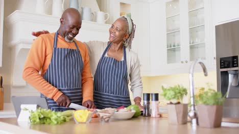 Pareja-De-Ancianos-Afroamericanos-En-Delantales-Preparando-Comida-Usando-Tableta-En-La-Cocina,-Cámara-Lenta