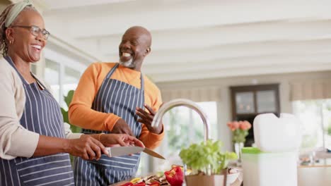 Fröhliches-Afroamerikanisches-Seniorenpaar-In-Schürzen,-Das-Essen-In-Der-Küche-Zubereitet,-Zeitlupe