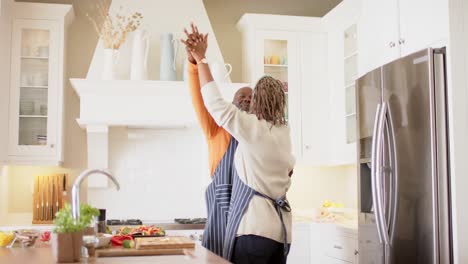 Happy-african-american-senior-couple-in-aprons-dancing-in-kitchen,-slow-motion