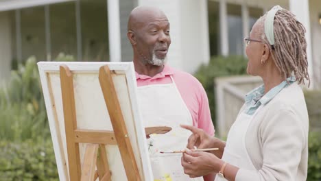 Glückliches-älteres-Afroamerikanisches-Paar-Malt-Auf-Holzstaffelei-Im-Garten,-Zeitlupe