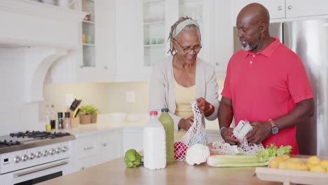 Feliz-Pareja-De-Ancianos-Afroamericanos-Desempacando-Comestibles-En-La-Cocina,-Cámara-Lenta