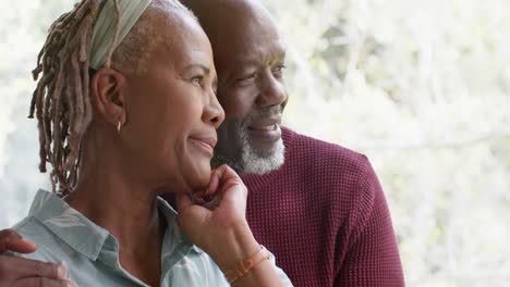 Reflexiva-Pareja-De-Ancianos-Afroamericanos-Abrazándose-Y-Mirando-Por-La-Ventana-En-Casa,-Cámara-Lenta