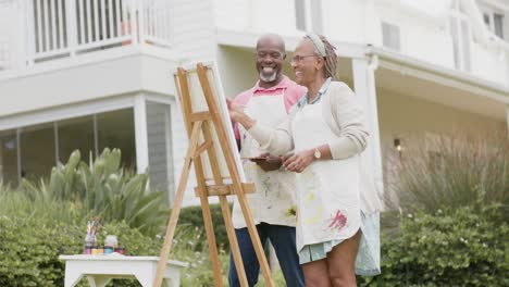 Happy-senior-african-american-couple-painting-on-wooden-easel-in-garden,-slow-motion