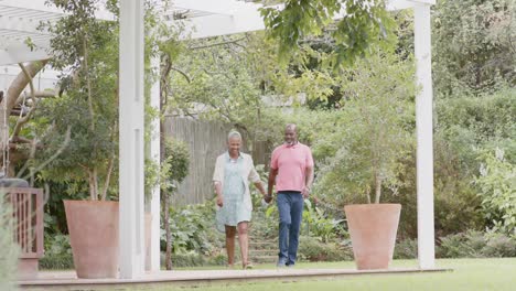 Happy-senior-african-american-couple-holding-hands-and-walking-in-garden,-slow-motion