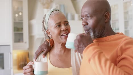 Glückliches-Afroamerikanisches-Seniorenpaar,-Das-Sich-In-Der-Küche-Umarmt-Und-Kaffee-Trinkt,-Zeitlupe