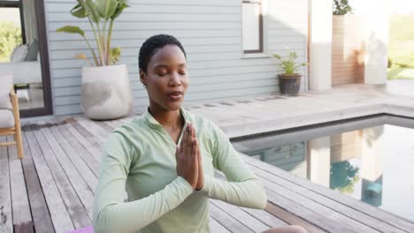 Focused-biracial-woman-practicing-yoga-and-meditating-at-pool-in-garden,-slow-motion