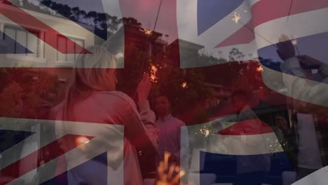 Animation-of-flag-of-united-kingdom-waving-over-diverse-friends-dancing-with-sparkles-stick-at-beach
