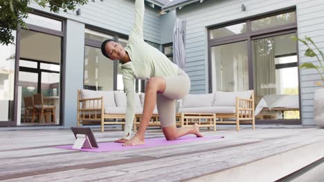 Konzentrierte-Biracial-Frau-Praktiziert-Yoga-Und-Stretching-Mit-Tablet-Im-Garten,-Zeitlupe