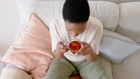Glückliche-Afroamerikanische-Frau-Sitzt-Auf-Dem-Sofa,-Trinkt-Tee,-Zeitlupe