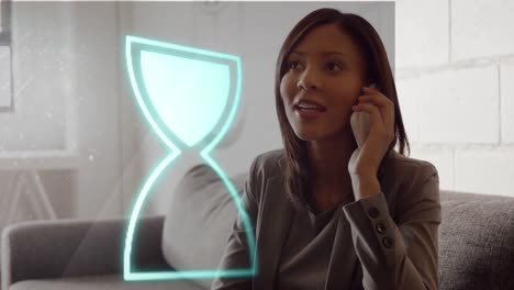 Animation-of-neon-hour-glass-icon-against-biracial-businesswoman-talking-on-smartphone-at-office