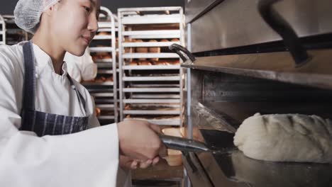 Diverse-bakers-working-in-bakery-kitchen,-putting-bread-into-oven-in-slow-motion