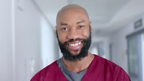 Portrait-of-happy-african-american-male-doctor-wearing-scrubs-in-corridor,-slow-motion