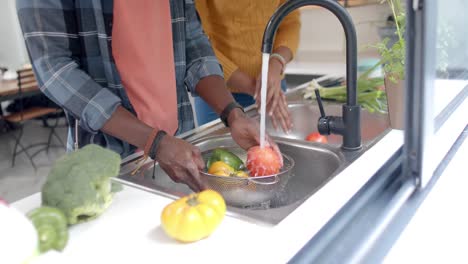 Mid-section-of-african-american-couple-rinsing-vegetables-in-kitchen,-slow-motion