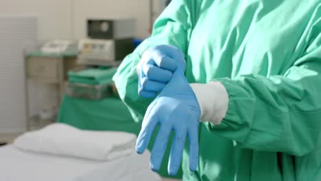 Midsection-of-caucasian-female-surgeon-wearing-medical-gloves-in-operating-theatre,-slow-motion