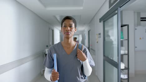 African-american-female-doctor-wearing-scrubs-and-walking-in-corridor,-slow-motion