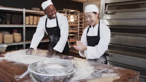 Happy-diverse-bakers-working-in-bakery-kitchen,-rolling-dough-on-counter-in-slow-motion