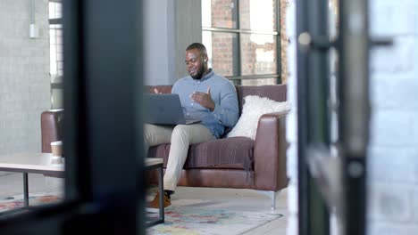 Glücklicher-Afroamerikanischer-Gelegenheitsgeschäftsmann-Mit-Laptop-Videoanruf-Auf-Der-Couch,-Kopierraum,-Zeitlupe