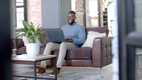 Happy-african-american-casual-businessman-having-laptop-video-call-on-couch,-copy-space,-slow-motion