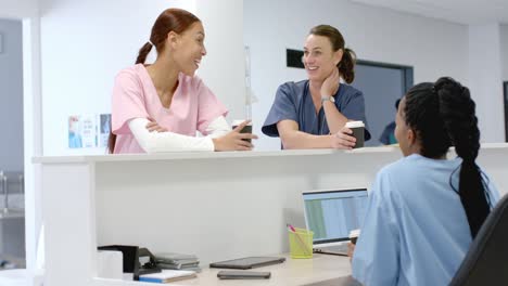 Diverse-doctors-talking-to-medical-recepcionist-sitting-at-front-desk-at-hospital,-slow-motion
