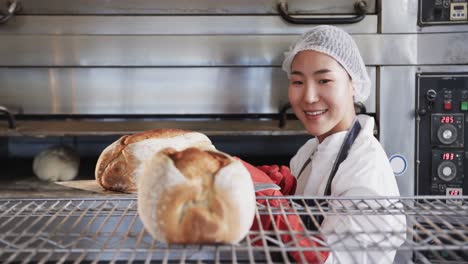 Fröhliche-Asiatische-Bäckerin,-Die-In-Der-Backküche-Arbeitet-Und-In-Zeitlupe-Frisches-Brot-Herausbringt