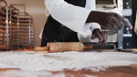 African-american-male-baker-working-in-bakery-kitchen,-rolling-dough-on-counter-in-slow-motion