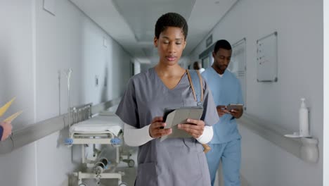 Portrait-of-african-american-female-doctor-wearing-scrubs,-using-tablet-in-corridor,-slow-motion