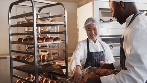 Happy-diverse-bakers-working-in-bakery-kitchen,-holding-fresh-bread-and-talking-in-slow-motion