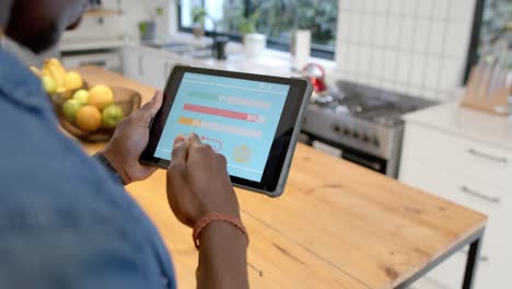 African-american-man-using-tablet-with-smart-home-interface-in-kitchen,-slow-motion