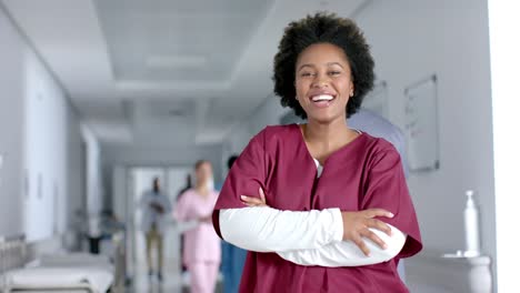 Portrait-of-happy-african-american-female-doctor-wearing-scrubs,-smiling-in-corridor,-slow-motion