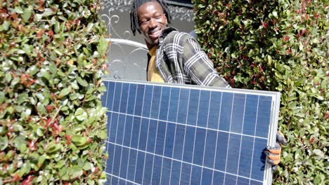 Feliz-Hombre-Afroamericano-Sosteniendo-Panel-Fotovoltaico-Entrando-A-La-Propiedad,-Cámara-Lenta