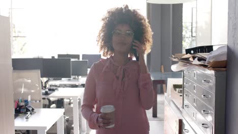 Happy-biracial-casual-businesswoman-walking-through-office-talking-on-smartphone,-slow-motion