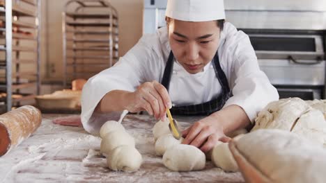 Panadera-Asiática-Enfocada-Trabajando-En-La-Cocina-De-Panadería,-Cortando-Masa-Para-Panecillos-En-Cámara-Lenta