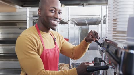 Porträt-Eines-Glücklichen-Afroamerikanischen-Männlichen-Barista,-Der-In-Zeitlupe-Kaffee-In-Einer-Bäckerei-Zubereitet