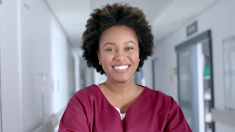 Portrait-of-happy-african-american-female-doctor-wearing-scrubs-in-corridor,-slow-motion