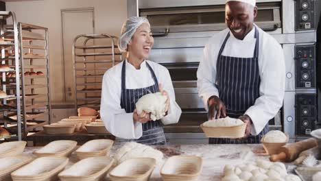 Happy-diverse-bakers-working-in-bakery-kitchen,-kneading-dough-for-bread-in-slow-motion