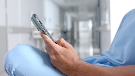 Midsection-of-biracial-male-doctor-using-smartphone-in-corridor,-slow-motion