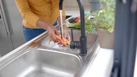 Mid-section-of-african-american-woman-rinsing-vegetables-in-kitchen,-slow-motion
