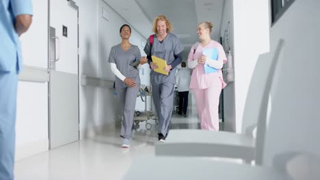 Happy-diverse-doctors-talking-and-walking-in-corridor-at-hospital,-slow-motion