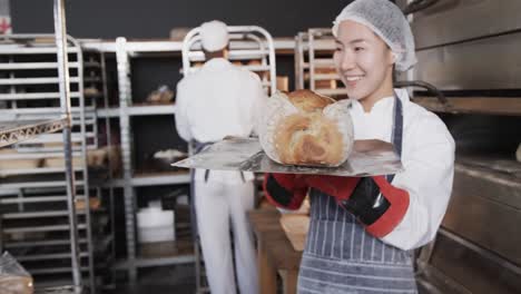 Happy-diverse-bakers-working-in-bakery-kitchen,-putting-fresh-bread-out-in-slow-motion