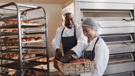 Portrait-of-happy-diverse-bakers-working-in-bakery-kitchen,-holding-fresh-bread-in-slow-motion