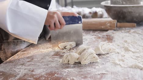 Asian-female-baker-working-in-bakery-kitchen,-cutting-dough-on-counter-in-slow-motion