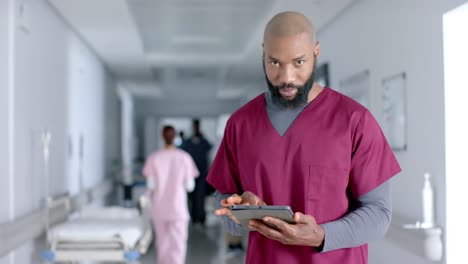 Porträt-Eines-Afroamerikanischen-Männlichen-Arztes,-Der-Peelings-Trägt-Und-Im-Flur-Ein-Tablet-Benutzt,-Zeitlupe