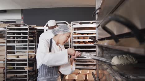Diverse-bakers-working-in-bakery-kitchen,-putting-bread-into-oven-in-slow-motion