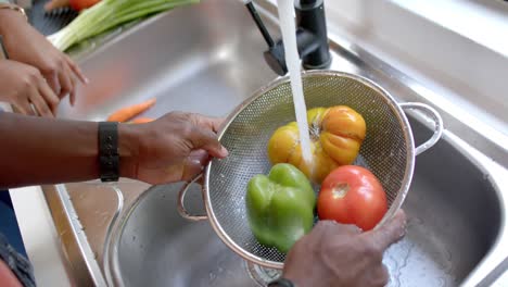 Hands-of-african-american-couple-rinsing-vegetables-in-kitchen,-slow-motion