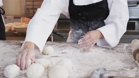Midsection-of-asian-female-baker-working-in-bakery-kitchen,-forming-rolls-from-dough,-slow-motion