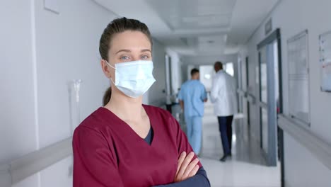 Portrait-of-happy-caucasian-female-doctor-wearing-face-mask-in-corridor,-slow-motion