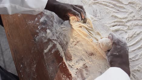 African-american-male-baker-working-in-bakery-kitchen,-kneading-dough-on-counter-in-slow-motion