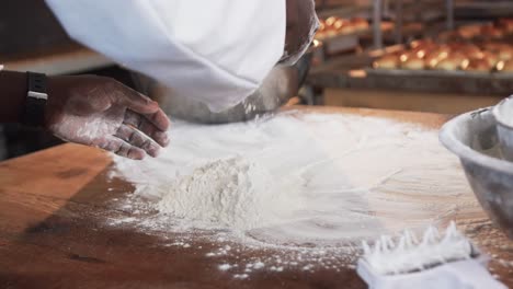 African-american-male-baker-working-in-bakery-kitchen,-pouring-flour-on-counter-in-slow-motion